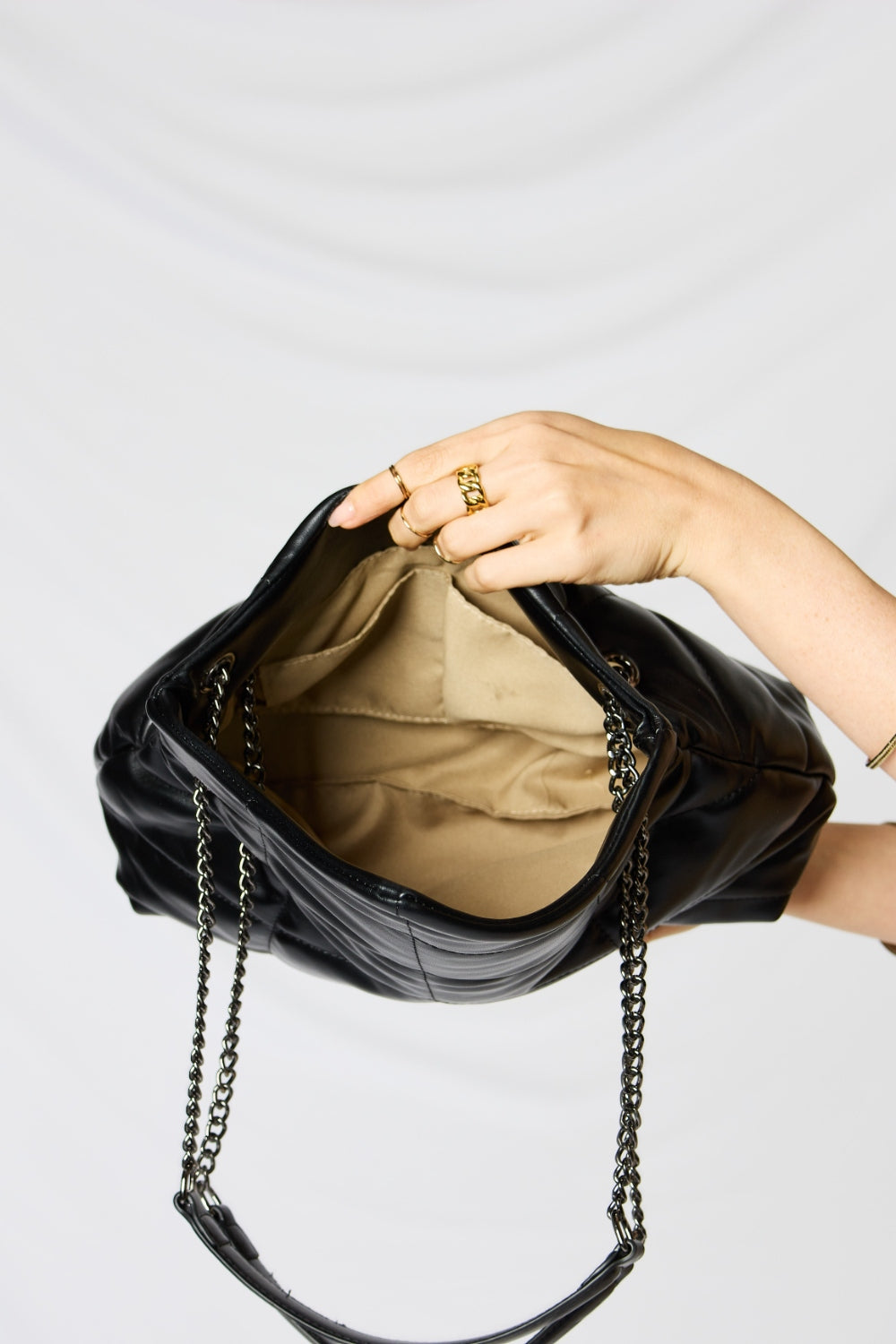 A person holding a stylish SHOMICO PU Leather Chain Handbag over their shoulder against a white background. They are dressed in a beige outfit and looking at the camera, embodying sustainable fashion.