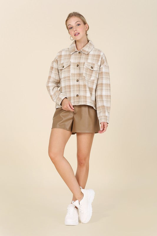 A person wearing a yellow plaid short shacket with pockets and blue jeans, highlighted by a crisp shirt collar, sits against a neutral backdrop.