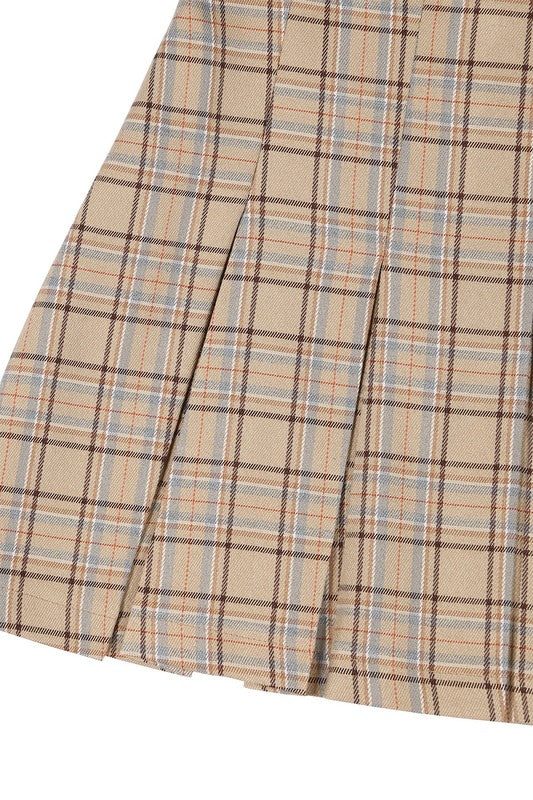 A person dressed in a plaid pleated mini skirt paired with a beige sweater is posed against a plain backdrop. This fashionable and versatile outfit, featuring the Plaid Pleated Mini Skirt, is designed for easy maintenance and can be machine washed in cold water.