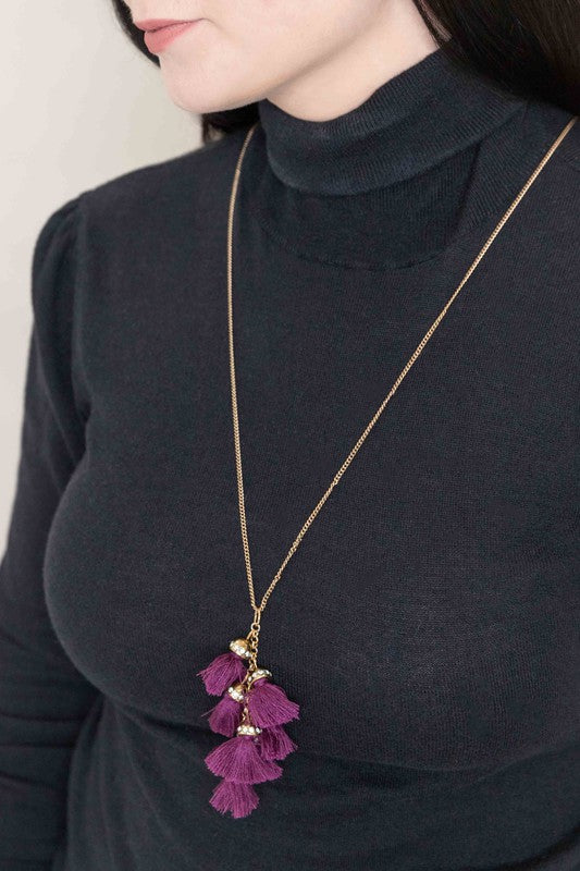 Bijou Tassel Necklace with red tassel pendant on a white background. This bohemian jewelry piece adds a vibrant touch to any ensemble.