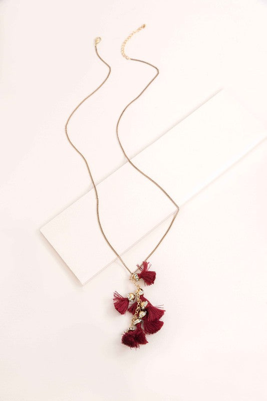 Bijou Tassel Necklace with red tassel pendant on a white background. This bohemian jewelry piece adds a vibrant touch to any ensemble.