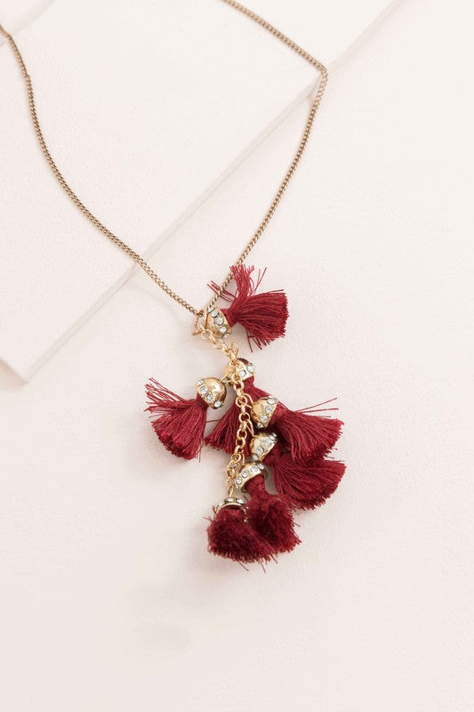 Bijou Tassel Necklace with red tassel pendant on a white background. This bohemian jewelry piece adds a vibrant touch to any ensemble.