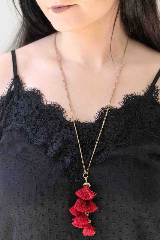 Bijou Tassel Necklace with red tassel pendant on a white background. This bohemian jewelry piece adds a vibrant touch to any ensemble.