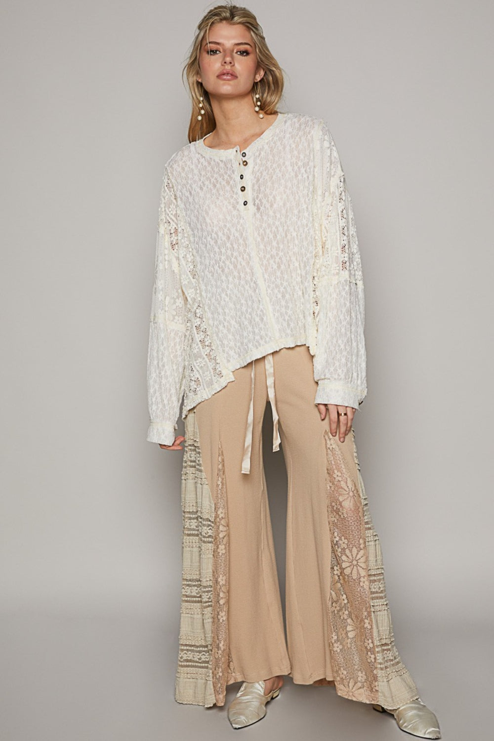 A woman is wearing the POL Round Neck Long Sleeve Raw Edge Lace Top, paired with beige pants, as she stands against a neutral background.