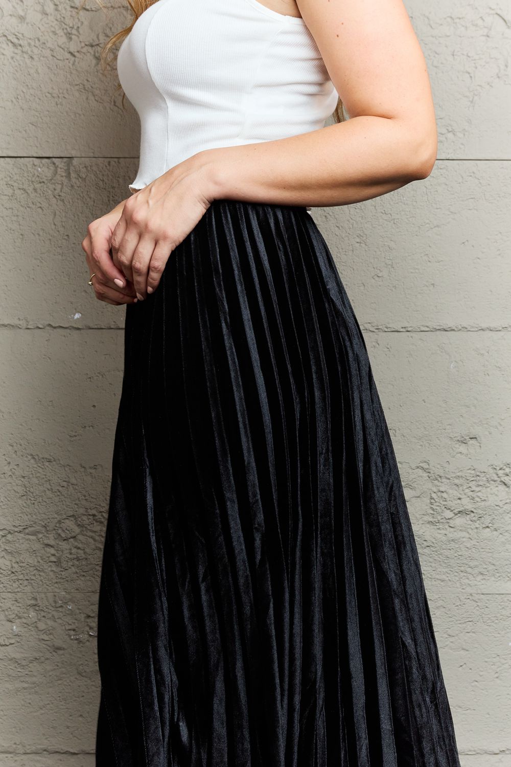 Person wearing a white sleeveless top, an elegant Ninexis Accordion Pleated Flowy Midi Skirt, and black platform sandals stands against a textured gray wall.