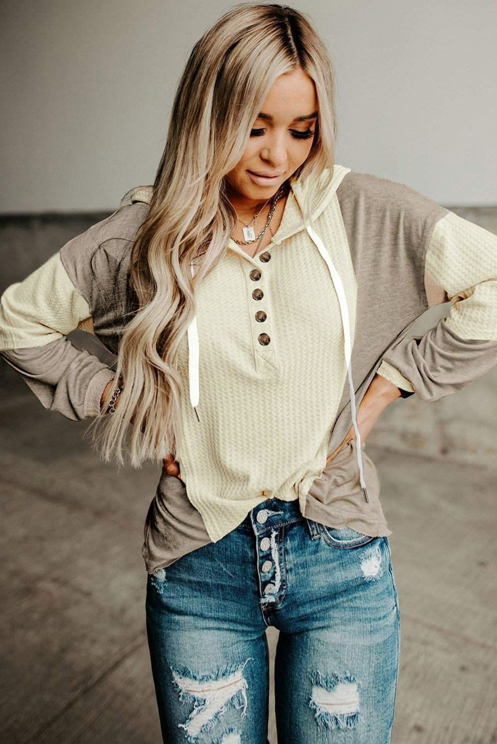 A person with long hair is seen from the back wearing an Apricot Contrast Block Waffle Knit Hoodie in cream and gray, paired with distressed denim jeans.