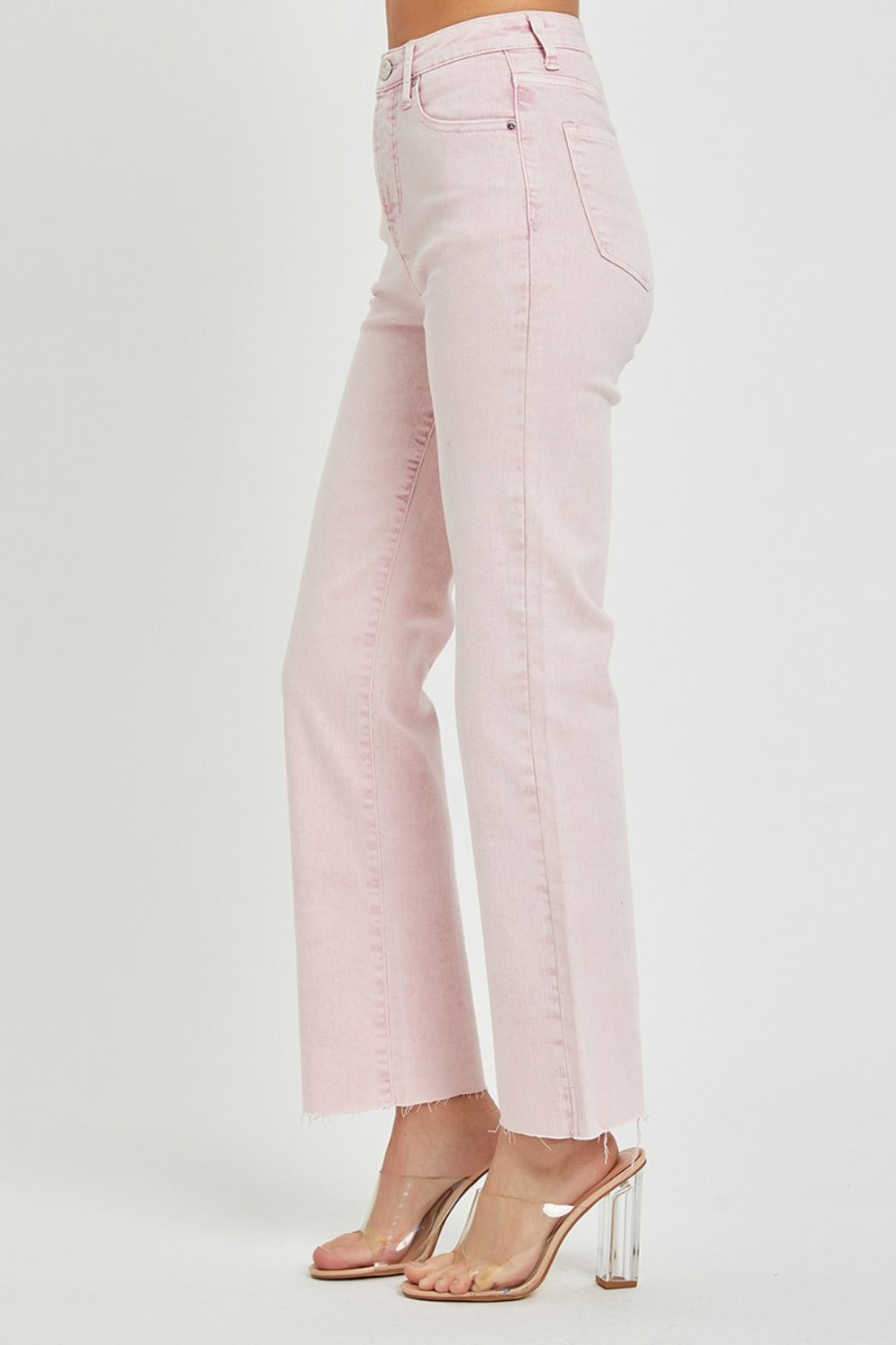 Person wearing RISEN Full Size High Rise Tummy Control Straight Jeans in light pink with a raw hem and clear heeled shoes against a plain white background.