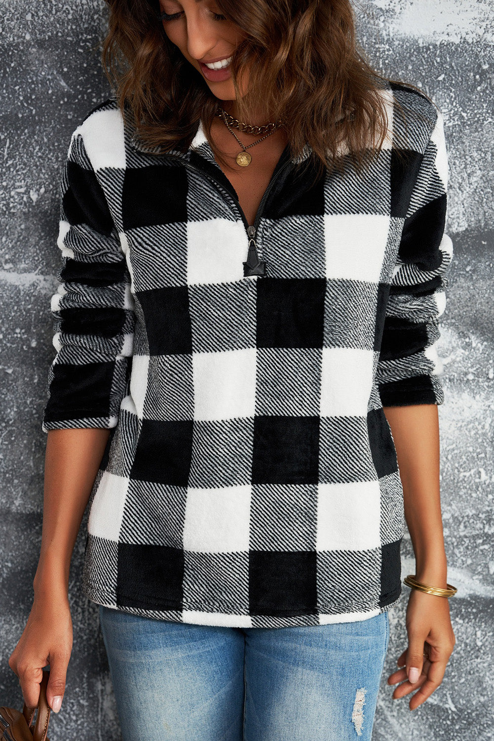 A woman with wavy hair is wearing a cozy Black Plaid Print 1/4 Zip Turn-down Collar Sweatshirt and blue jeans, standing with her back to the camera against a textured gray background.