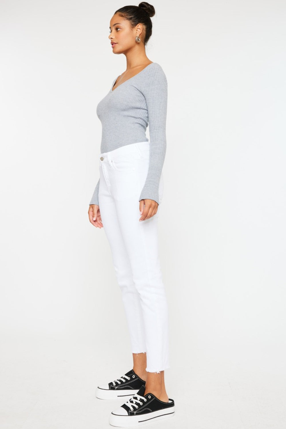 A person models a versatile gray long-sleeve top paired with flattering fit Kancan Mid Rise Ankle Skinny Jeans and sleek black sneakers, all set against a pristine white background.