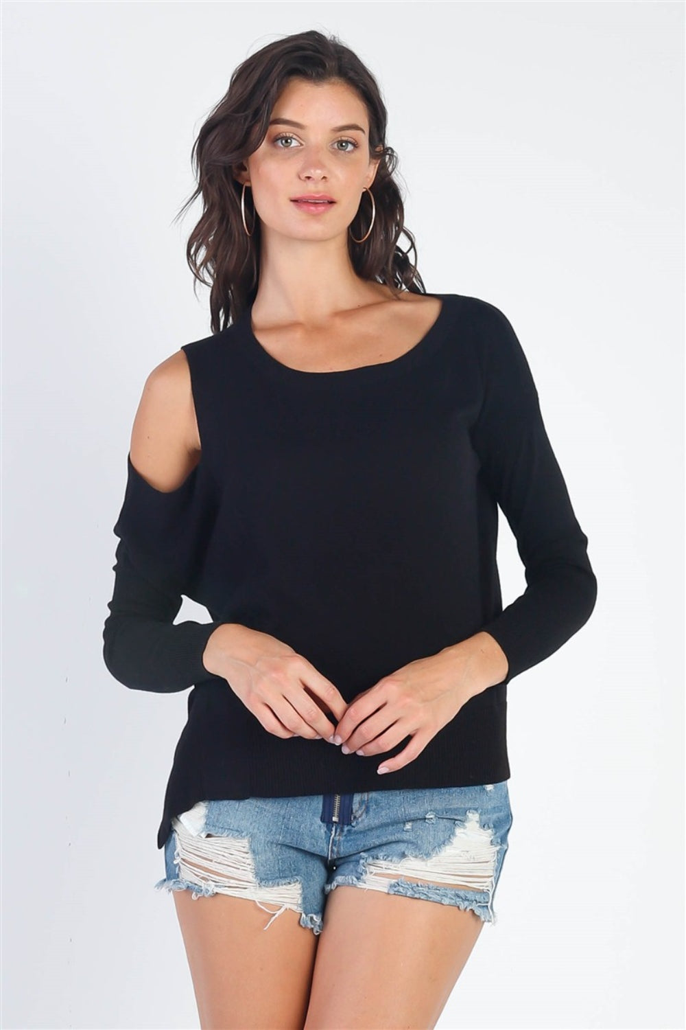 A person wearing the UNIQ Cold Shoulder Long Sleeve Knit Top in black and distressed denim shorts stands against a plain white background, effortlessly showcasing a versatile wardrobe choice.