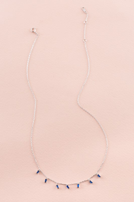 Sapphire Falls Necklace with sapphire gemstones pendants on a pink background.