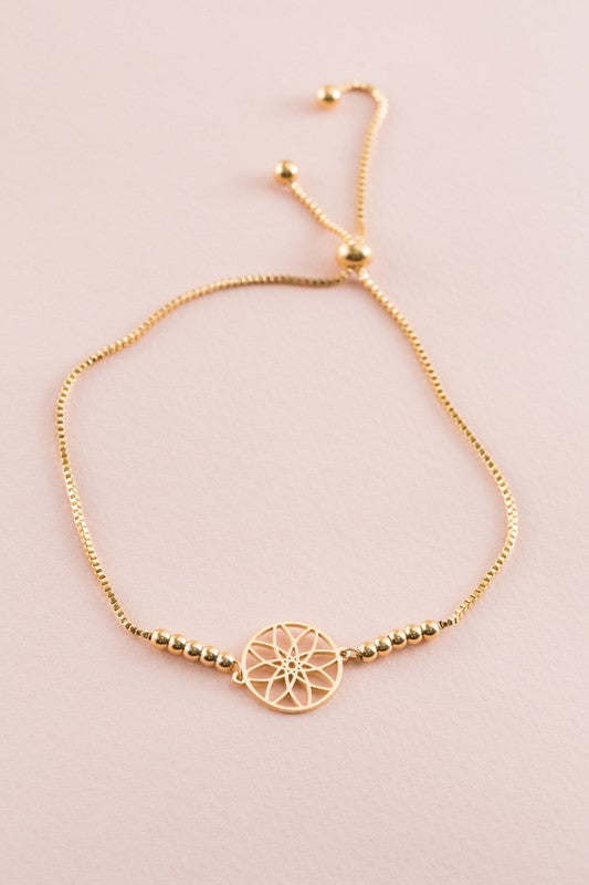 Seed of Life Bolo Bracelet with 14k gold plating, featuring a circular pendant and decorative beads on a pink background.