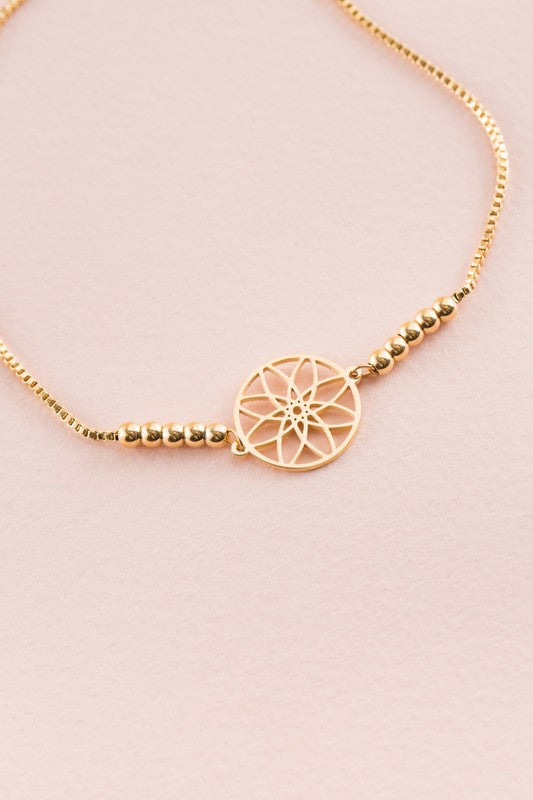 Seed of Life Bolo Bracelet with 14k gold plating, featuring a circular pendant and decorative beads on a pink background.