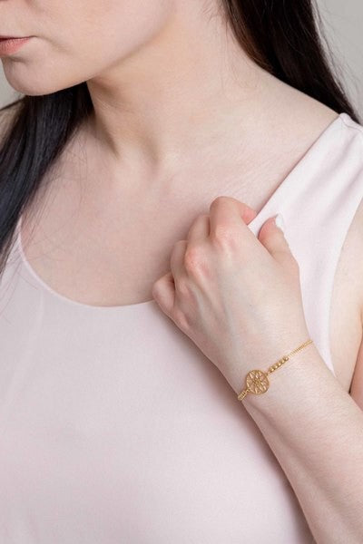 Seed of Life Bolo Bracelet with 14k gold plating, featuring a circular pendant and decorative beads on a pink background.