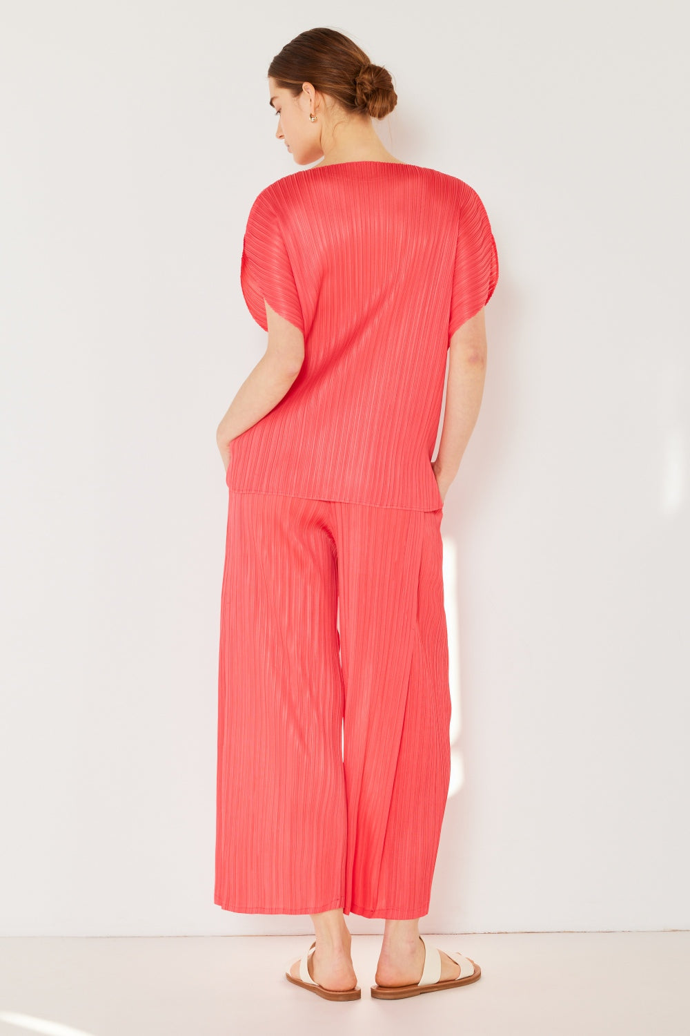 A person wearing the Marina West Swim Pleated Wide-Leg Pants with side pleat detail in red, standing against a white background with hands in pockets and wearing white sandals.