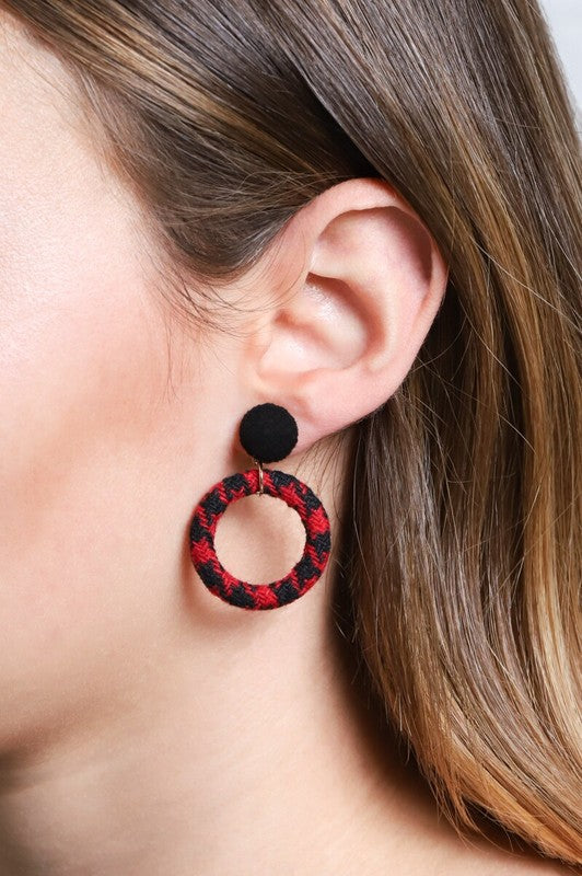 A pair of Go Getter Houndstooth Earrings with a black pompom on a white background.