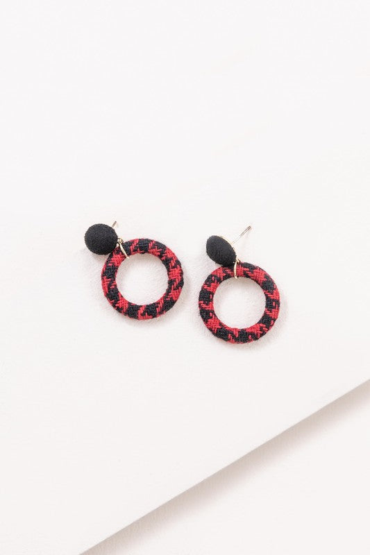 A pair of Go Getter Houndstooth Earrings with a black pompom on a white background.