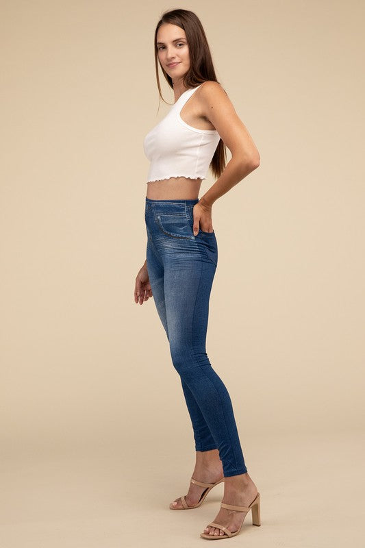 A person wearing Denim Leggings in a high-waisted black design and paired with black heels poses against a plain beige background, highlighting the sleek, stretchy fit.