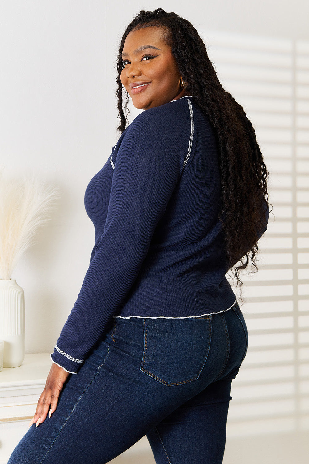 Person with long braided hair wearing a Basic Bae Long Raglan Sleeve Round Neck Top in navy blue and denim jeans, standing and smiling indoors.