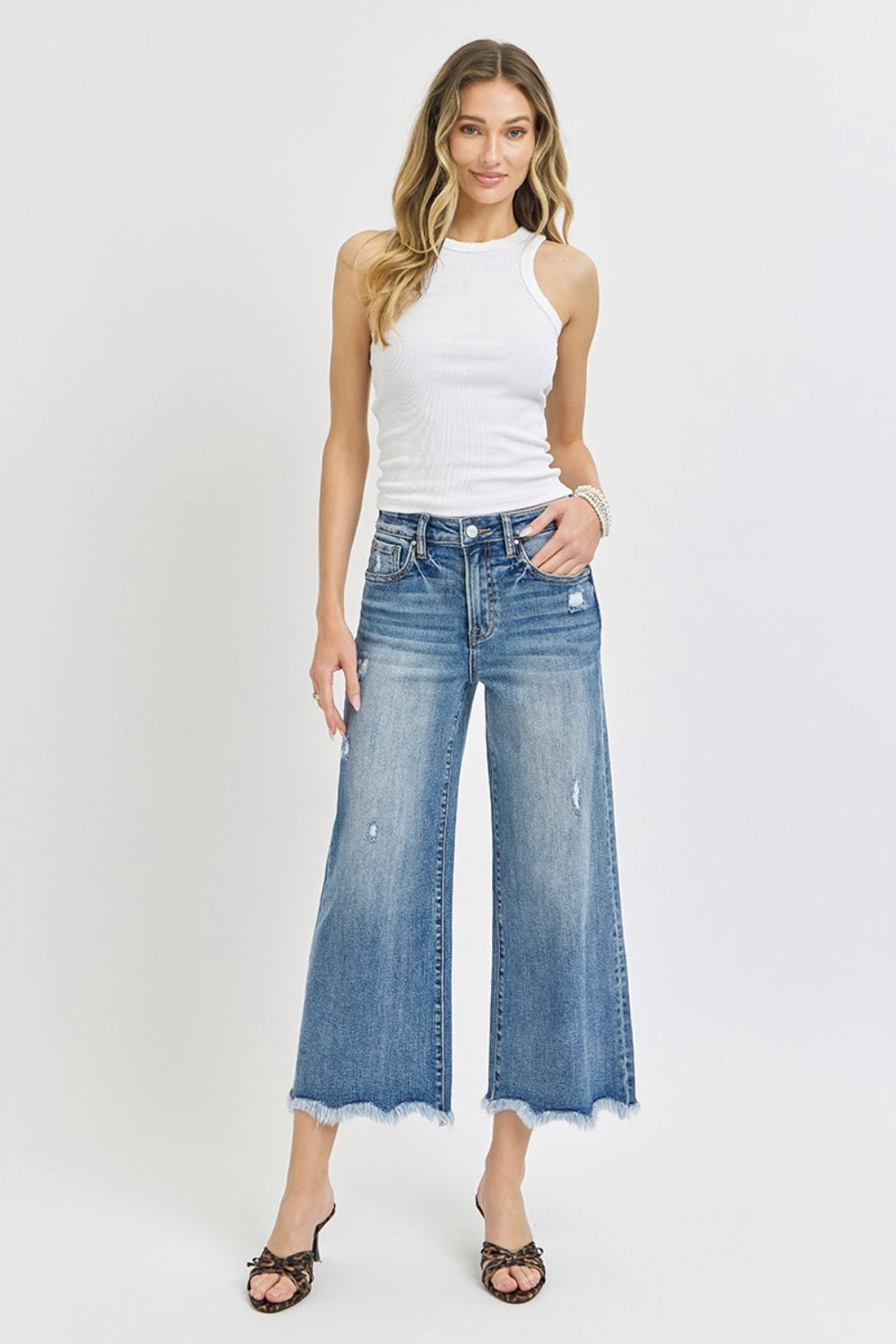 Person wearing Risen High Rise Cropped Flare Jeans with frayed details and a few rips, paired with strappy high-heeled sandals against a plain background.