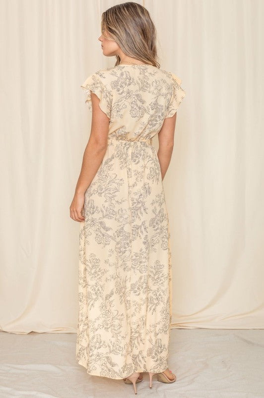 A woman in a long Floral Surplice Sash Sundress with no lining, made in the United States, stands casually in a room with contemporary furniture and large windows.