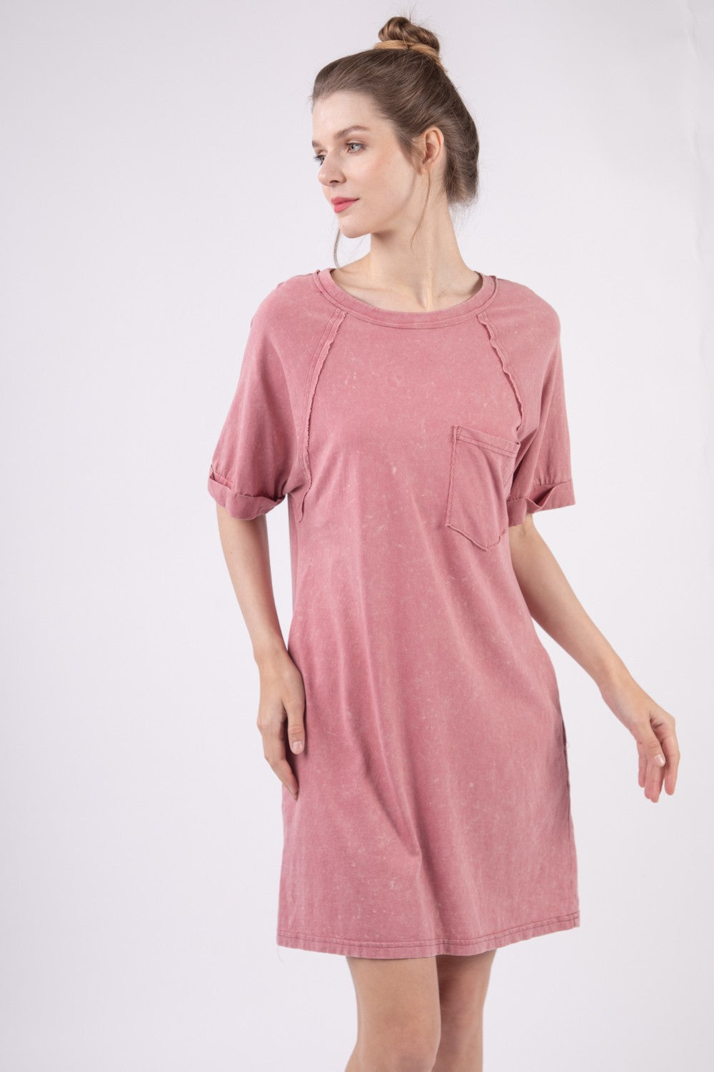 Wearing the VERY J Washed Round Neck Mini Tee Dress in pink, a person stands sideways against a plain background, effortlessly showcasing their casual wardrobe style.