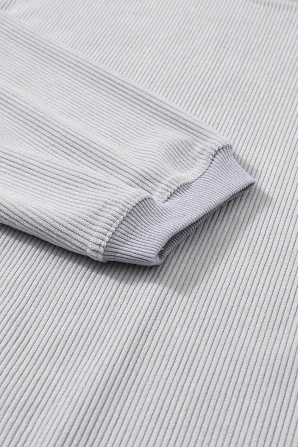 A woman wearing the Light Grey Ribbed Corduroy Oversized Sweatshirt with loose long sleeves, designed in corded fabric, making it fashionable for all body shapes.