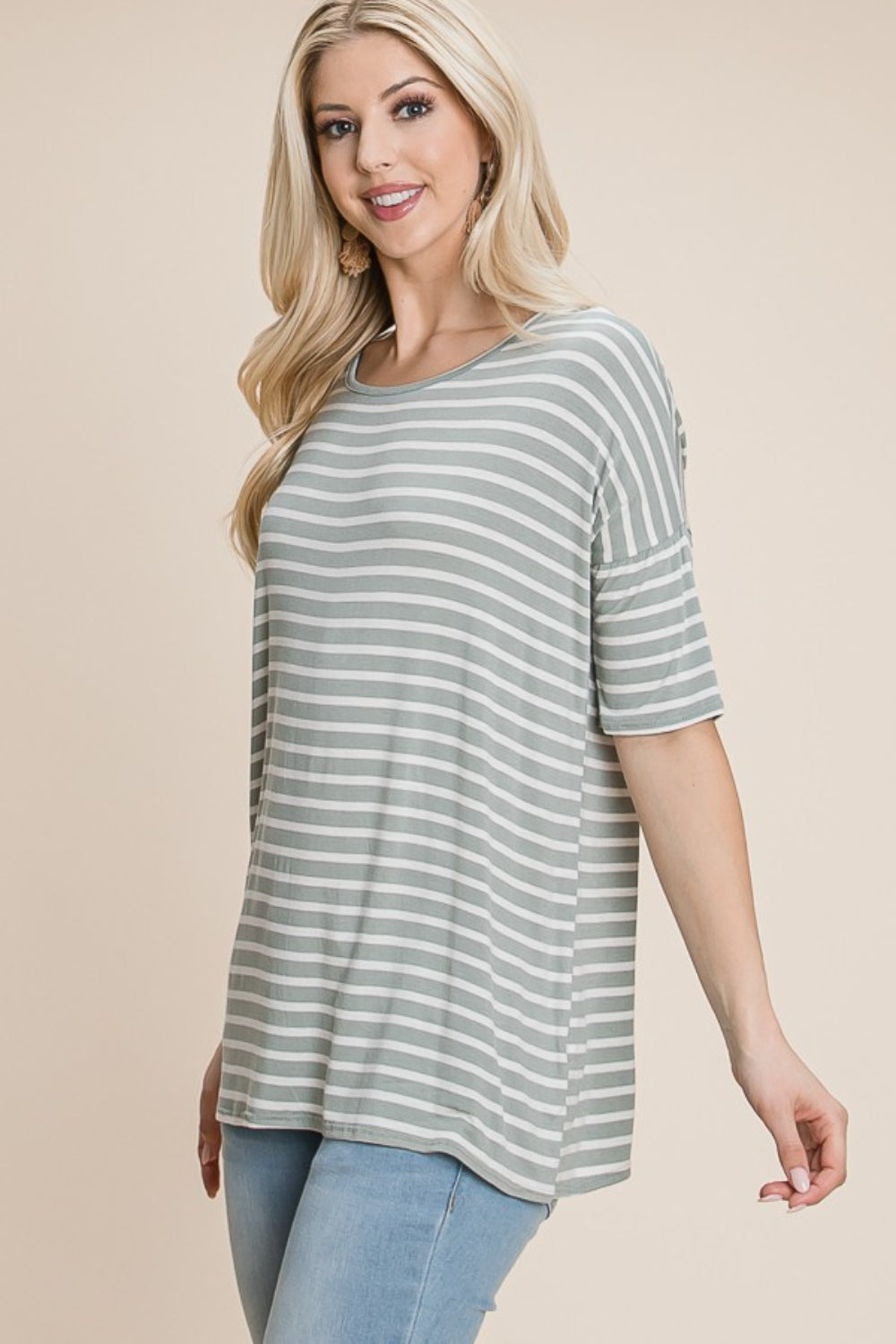 A woman with long blonde hair, dressed in a BOMBOM Striped Round Neck T-Shirt and blue jeans, exudes nautical charm while smiling and looking off to the side.