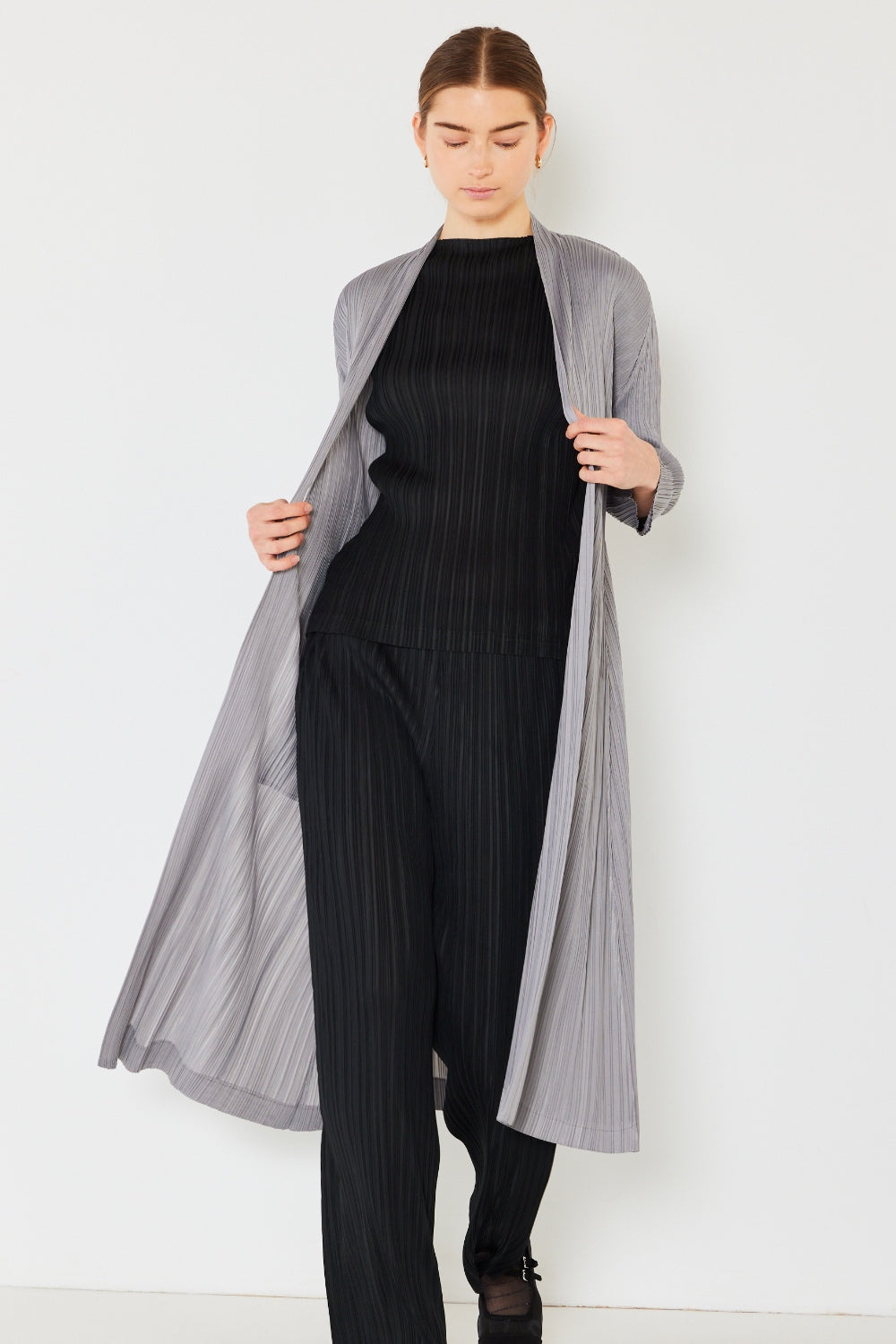 A person wears the Marina West Swim Pleated Long Sleeve Cardigan over a matching top and gray wide-leg pants, standing against a plain light background. This versatile layering piece, with its chic pleated long sleeves, adds an elegant touch to the ensemble.