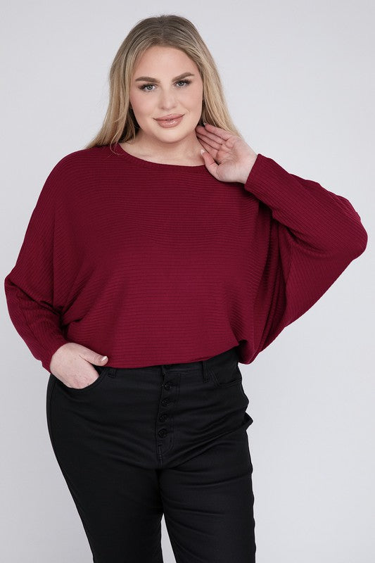 A woman wearing a Plus Ribbed Batwing Long Sleeve Boat Neck Sweater in red and black pants, standing and posing with her hand on her neck, smiling gently at the camera.