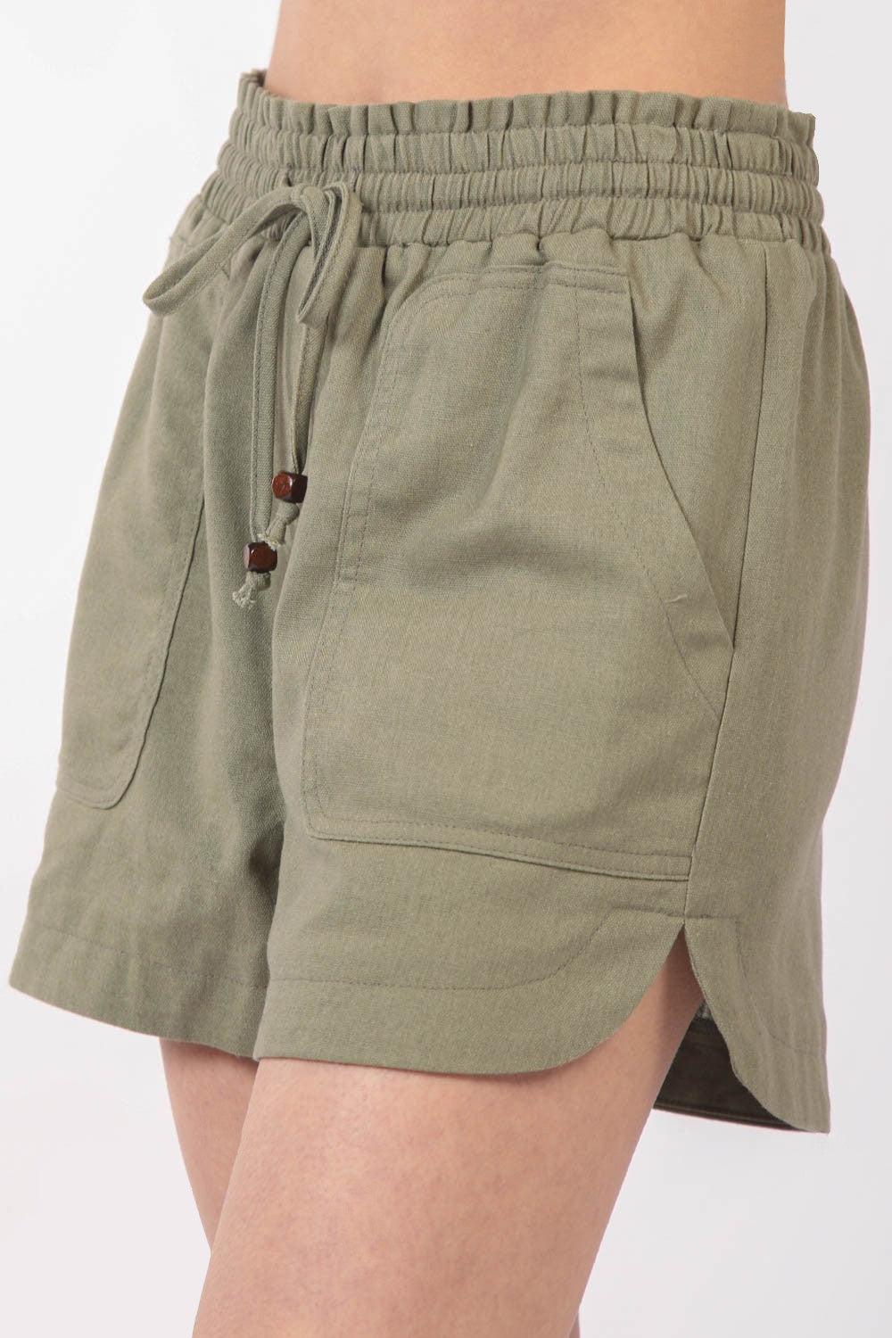 Close-up of a person wearing VERY J Drawstring Elastic Waist Linen Shorts in olive green, featuring two front pockets.