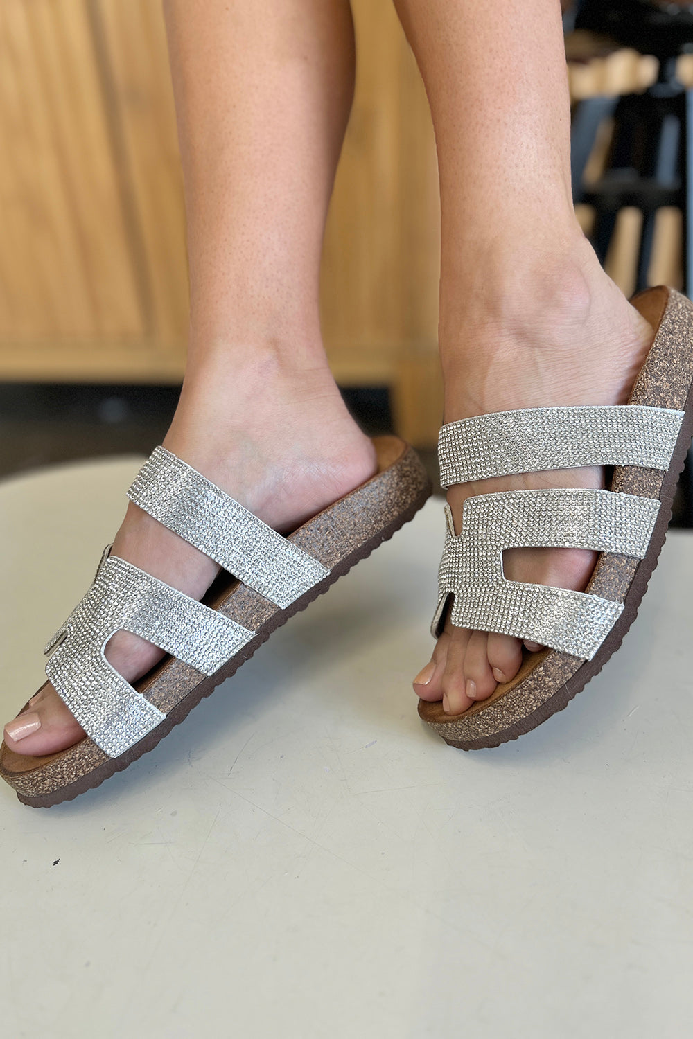 Close-up of a person's feet wearing glamorous, Forever Link Rhinestone Open Toe Sandals with silver texture and cork soles.