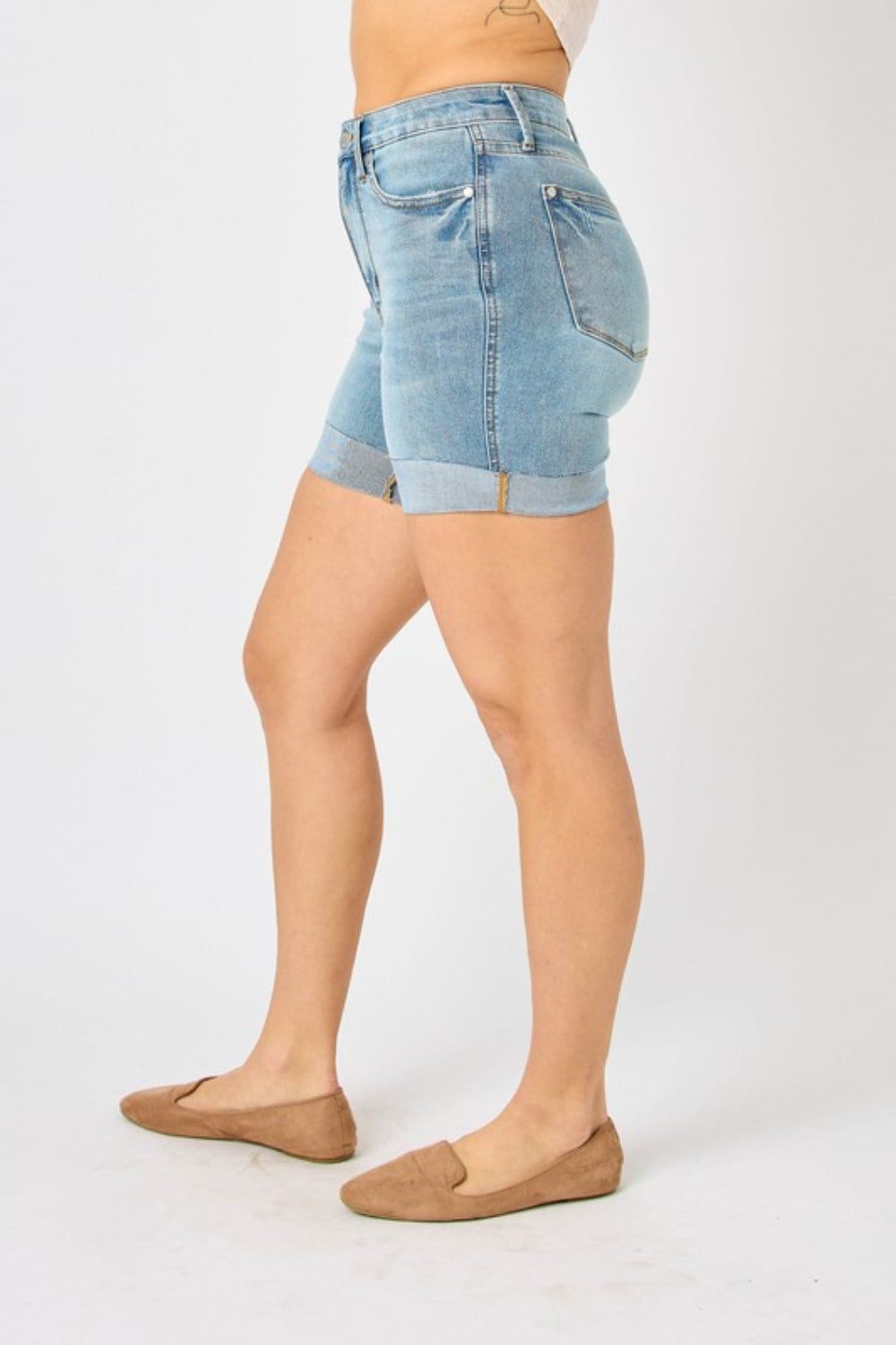 Person wearing Judy Blue Full Size Tummy Control Denim Shorts, which have a flattering fit, paired with brown shoes against a plain white background.