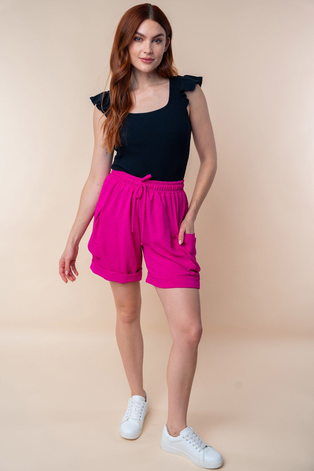 A person is wearing the White Birch High Waisted Drawstring Knit Cargo Shorts in bright pink, featuring side pockets and a drawstring waistband.