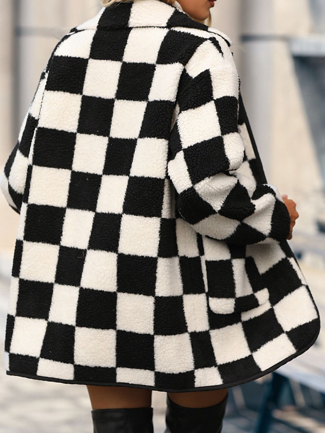 A person wearing the Double Take Full Size Checkered Button Front Coat with Pockets, a white turtleneck sweater, black shorts, and two gold necklaces holds a paper cup. The coat is Basic style and made from 100% polyester.