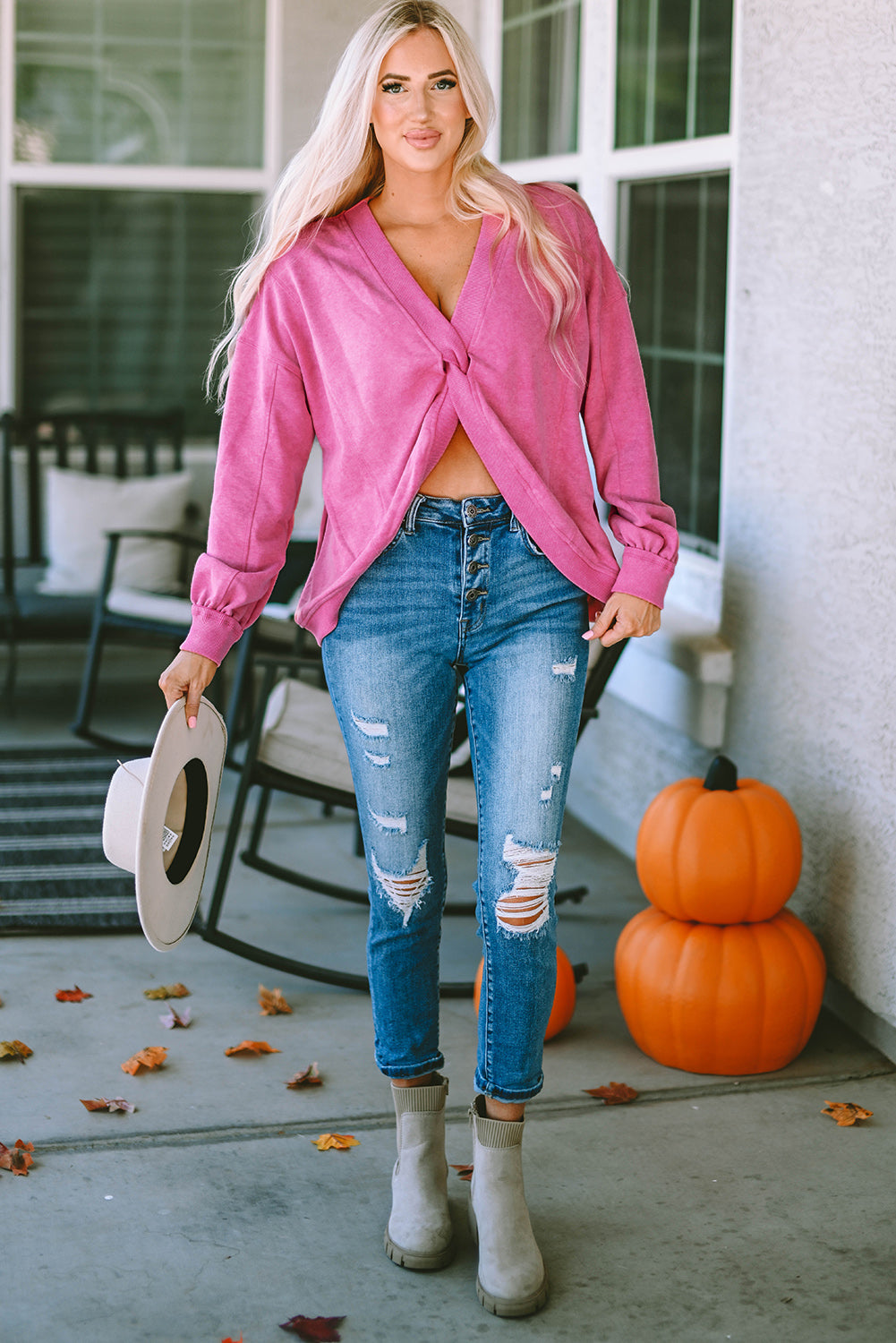 A woman stands with her back to the camera, wearing a long-sleeved Rose Exposed Seam Twist Open Back Oversized Sweatshirt and light blue jeans, showcasing a relaxed fit.