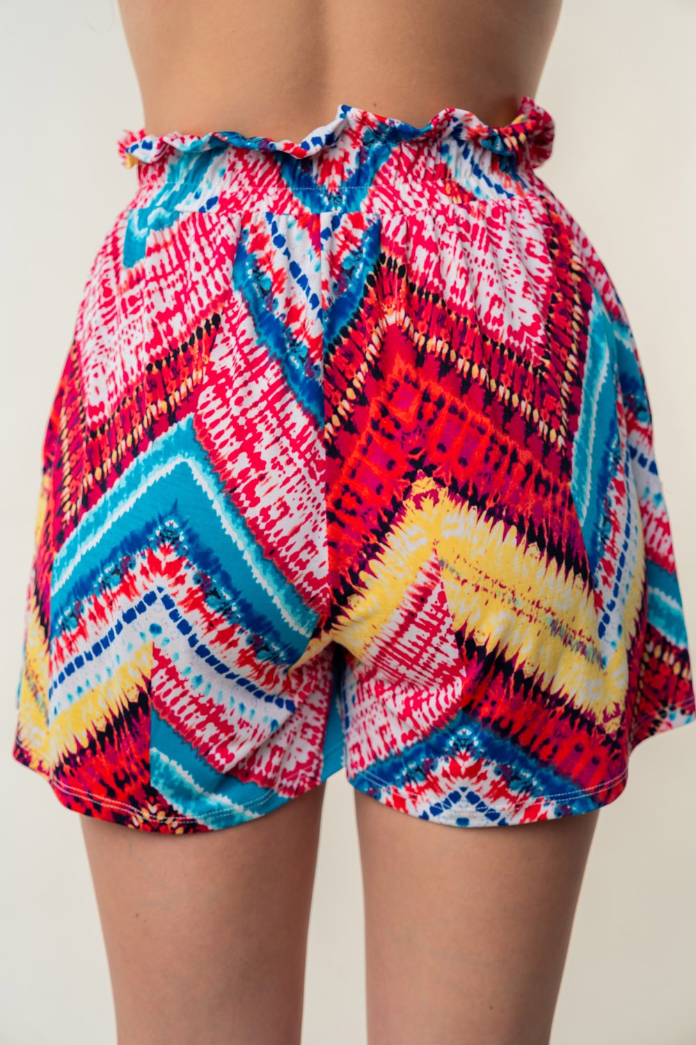 Close-up of a person wearing the White Birch High Waisted Printed Shorts, showcasing vibrant blue, pink, and yellow zigzag designs on lightweight slinky knit fabric with an adjustable waist-tie.