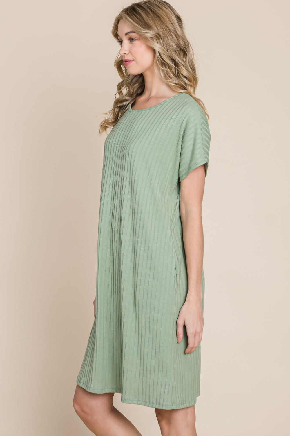 Against a beige background, a person is dressed in the BOMBOM Ribbed Round Neck Short Sleeve Dress in green, featuring a pocket.