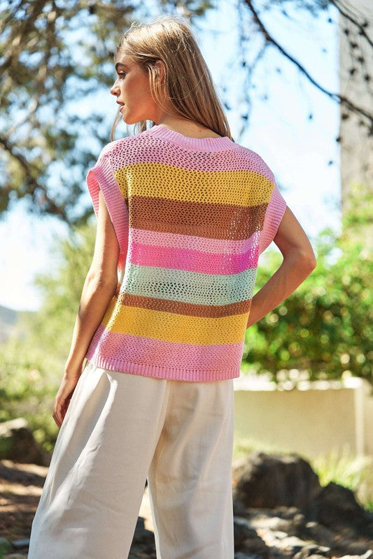 A woman outdoors wearing a Crochet Multi Striped Pullover Knit Sweater Vest and white pants, with her arms raised and eyes closed.