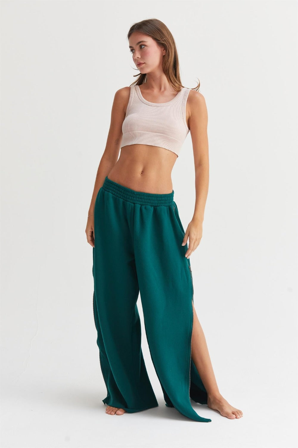 A person wearing a beige tank top and HYFVE Wide-Leg Side Zipper Sweatpants in teal.