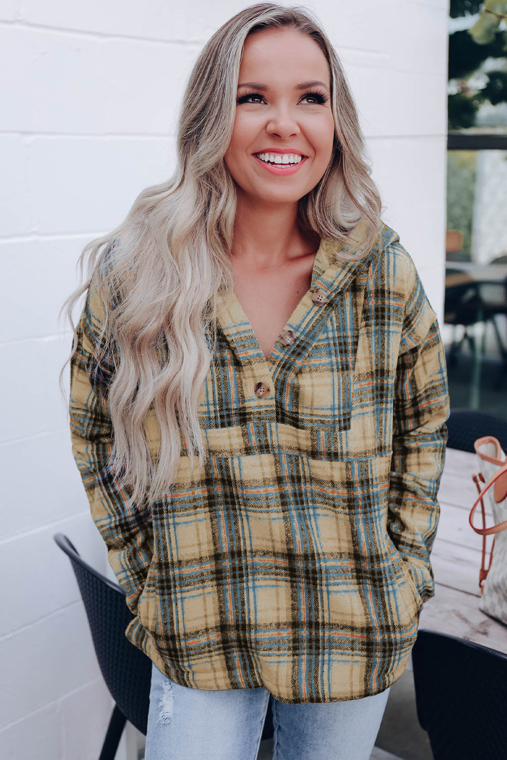 A person with long blonde hair, seen from the back, wearing a Khaki Plaid Button Neck Pocketed Pullover Hoodie and denim shorts, stands on a porch.