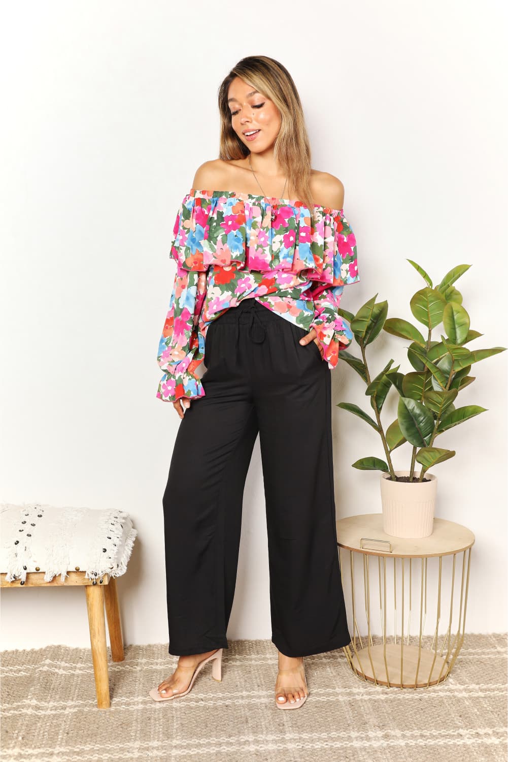 A person wearing a Floral Off-Shoulder Flounce Sleeve Layered Blouse and black pants stands in front of a plain white background.