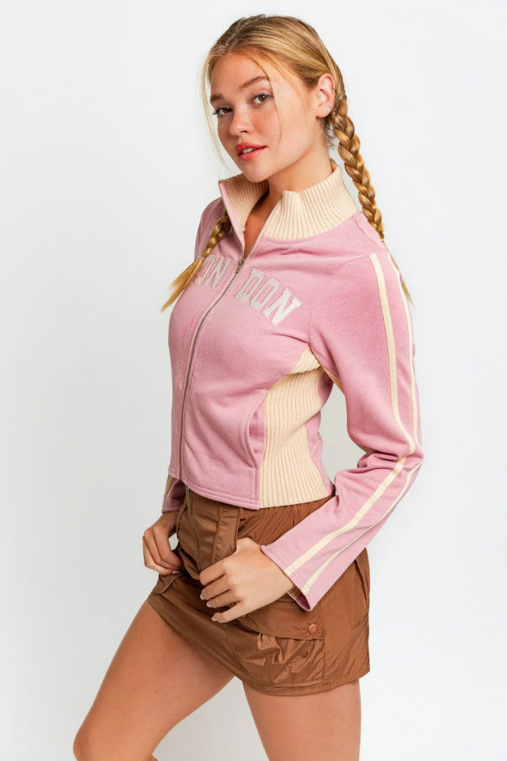 A person wearing the Le Lis Long Sleeve Mock Neck LONDON Embroidered Jacket in light pink and brown pants, looking to the side.