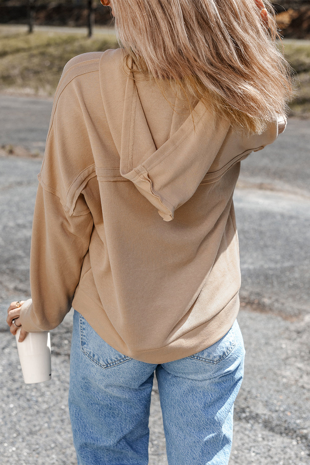 Person wearing a Khaki Casual Button Solid Patchwork Trim Hoodie and blue jeans is standing outdoors holding a white tumbler. The individual's blonde hair is partially visible from behind.