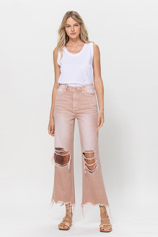 Person wearing 90's Vintage Crop Flare Jeans in rose pink with high waist, distressed details, rips on the knees, and frayed hems, paired with beige strappy sandals.