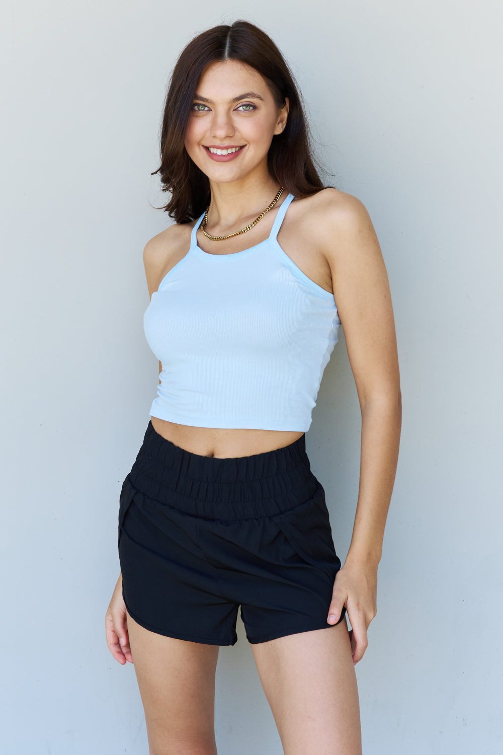 A woman wearing the Ninexis Everyday Staple Soft Modal Short Strap Ribbed Tank Top in Blue paired with black shorts smiles at the camera against a plain background.