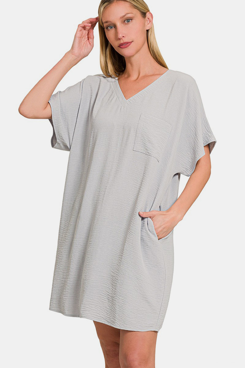 A person wearing the versatile light gray Zenana V-Neck Tee Dress with a chest pocket and a side pocket.