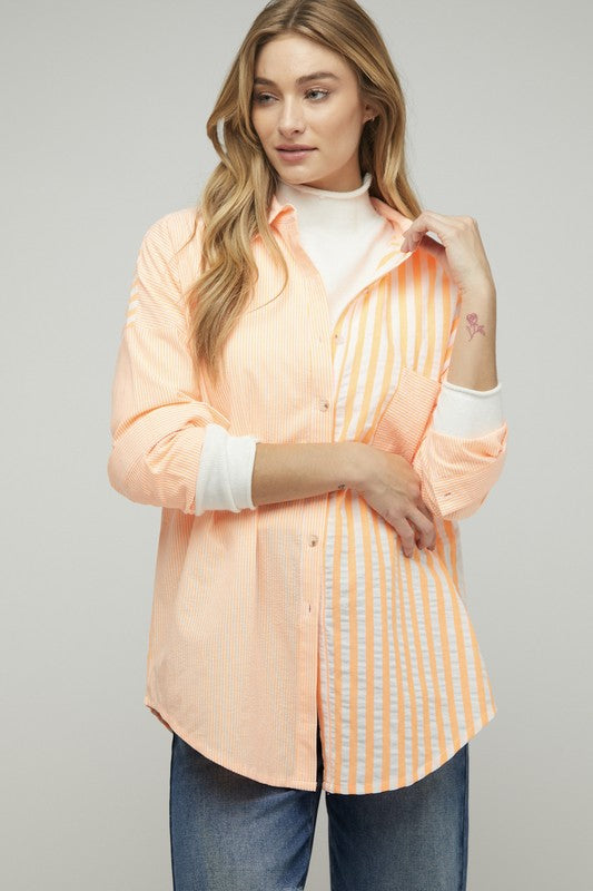 A person wearing a light pink Stripe Button Down Long Sleeve Shirt with rolled-up sleeves and jeans stands with their hands behind their head against a plain background.