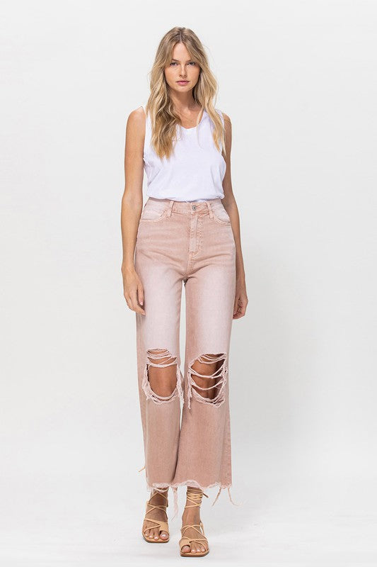 Person wearing 90's Vintage Crop Flare Jeans in rose pink with high waist, distressed details, rips on the knees, and frayed hems, paired with beige strappy sandals.