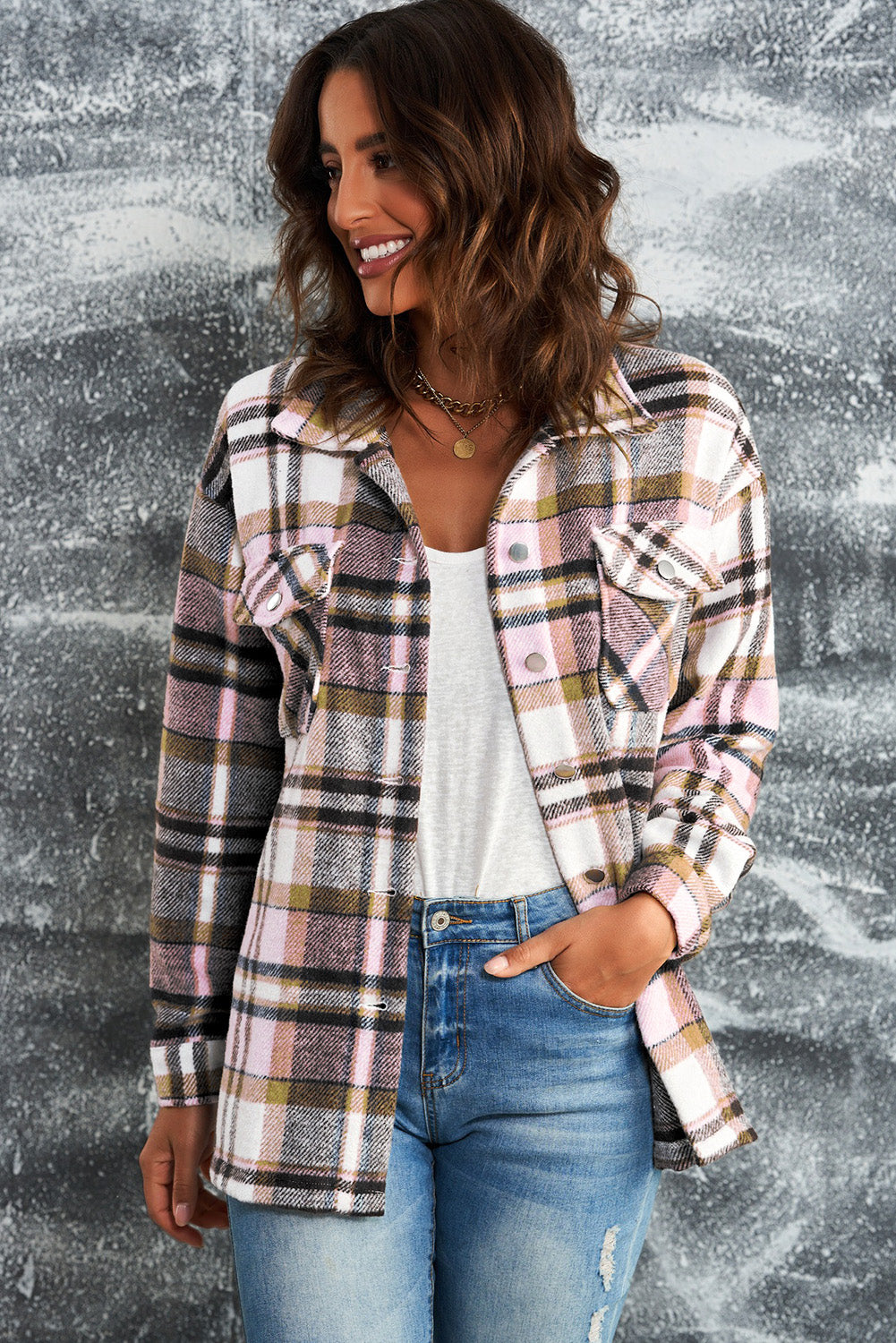 A person wearing a Brown Plaid Button Up Long Sleeve Flannel Shacket layered over a white top with ripped jeans and holding a brown handbag stands against a textured gray wall.